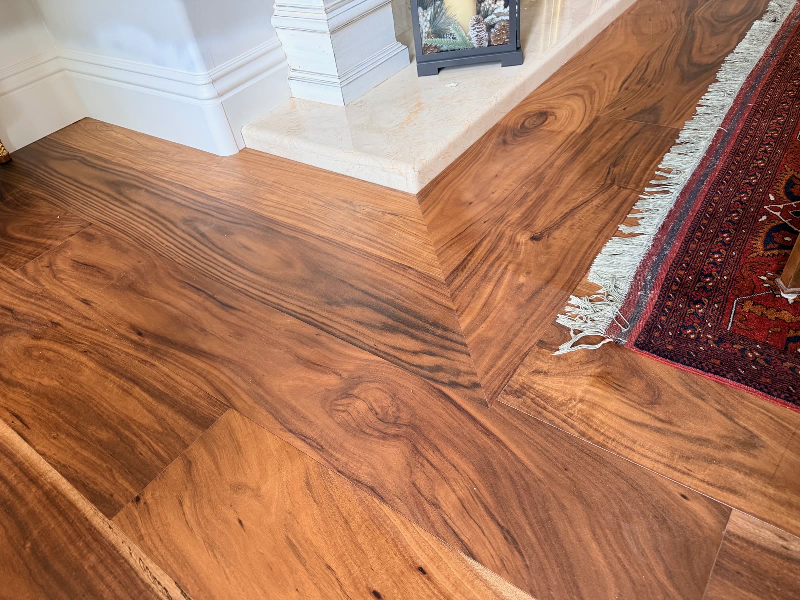 Highly figured acacia plank floor with a mitered border at a travertine hearth, Carmel Valley